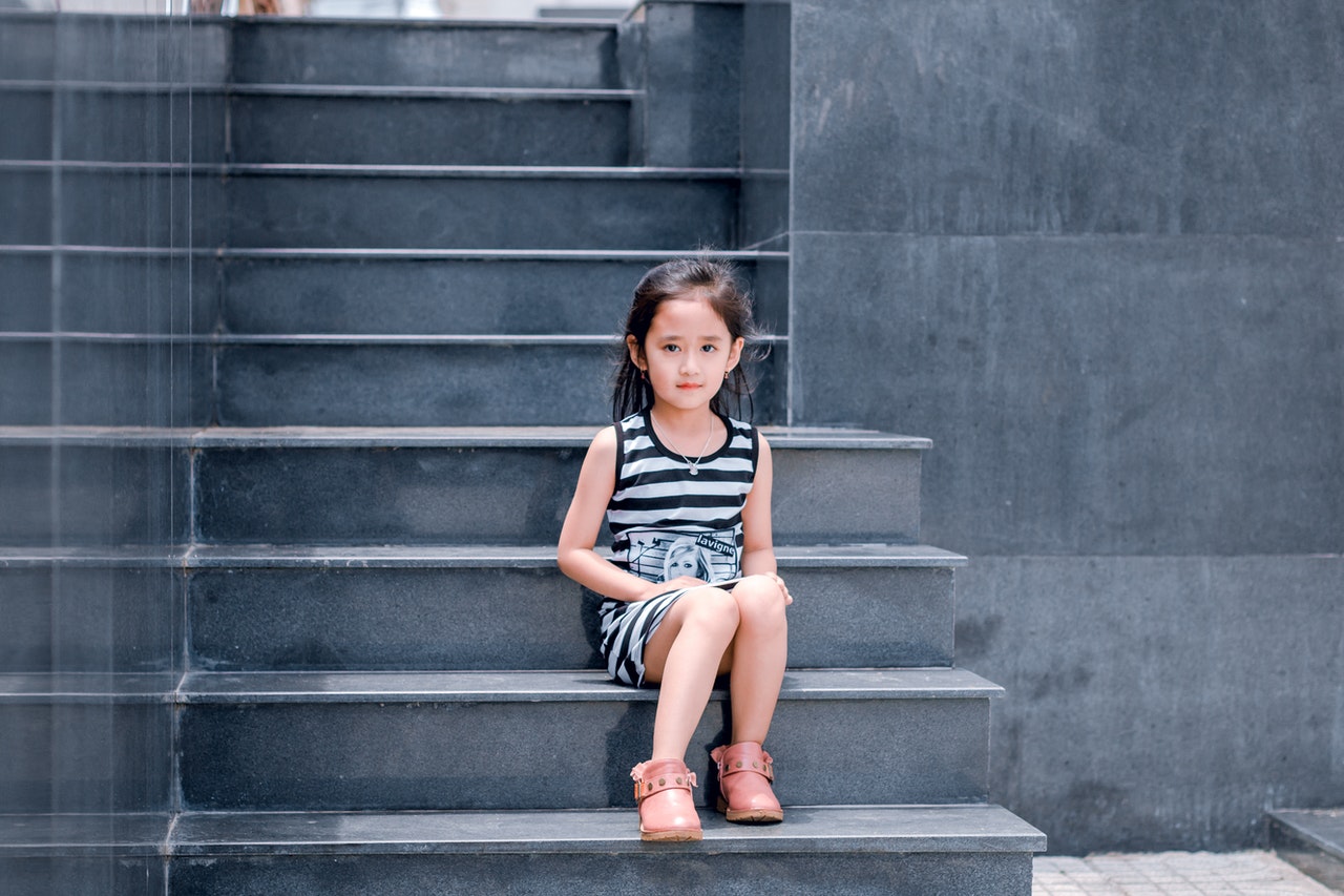 dziewczynka siedzi na schodach w różowych butach i sukience