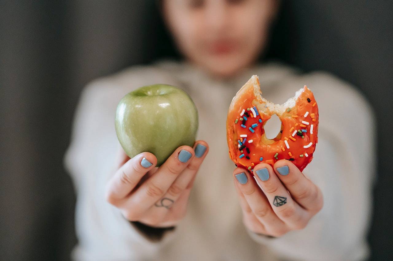 Dietetyczka w jednej dłoni trzyma jabłko a w drugiej pączka